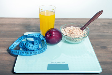 The concept of healthy diet, fitness and weight loss. Scales, measure tape, oatmeal, apple, a glass of juice on the table.