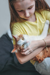 Cute tween girl in yellow t-shirt with her white cat at home