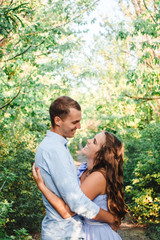 Fototapeta premium Couple in love smiling and hugging in trees tunnel. Man holding hands around woman. Tender and affectionate couple standing on nature background. Happy couple in love. Cope space