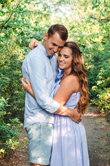 Fototapeta premium Couple in love smiling and hugging in trees tunnel. Man holding hands around woman. Tender and affectionate couple standing on nature background. Young beautiful couple. Happy couple in love