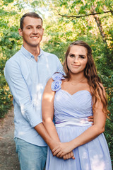 Fototapeta premium Couple in love smiling and hugging in trees tunnel. Man holding hands around woman. Tender and affectionate couple standing on nature background. Young beautiful couple. Happy couple in love