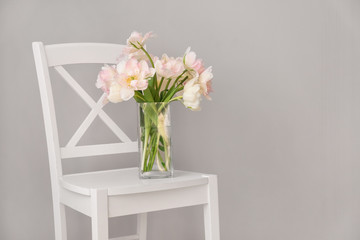 Bouquet of beautiful tulips on chair against grey background