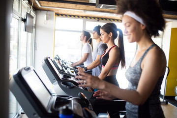 Fototapeta na wymiar Happy fit people running on treadmill at fitness gym club