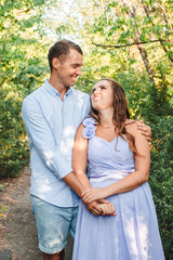 Fototapeta premium Couple in love smiling and hugging in trees tunnel. Man holding hands around woman. Tender and affectionate couple standing on nature background. Young beautiful couple. Happy couple in love