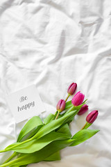 Bouquet of beautiful tulips and card with text BE HAPPY on bed