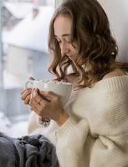 Girl sitting near the window, hold big white mag cacao with marshmallow. Home cozy lifestile photo