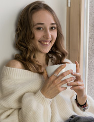 Girl sitting near the window, hold big white mag cacao with marshmallow. Home cozy lifestile photo