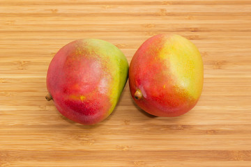 Two whole mango fruits on a wooden surface