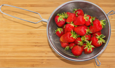 Washed strawberries in stainless steel sieve and bowl on table