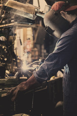 welder is welding metal part in garage. with protective mask, industrial steel welder