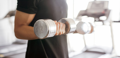 close up young man playing dumbbell curl for building bicep muscle at gym , lifestyle concept