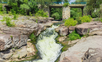 Fototapeta na wymiar Small waterfall on river flowing from under a stone bridge