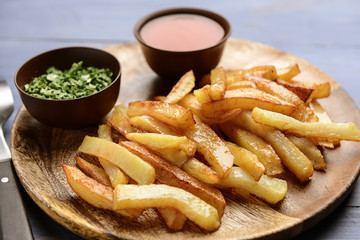 Plate with tasty french fries and sauce on table
