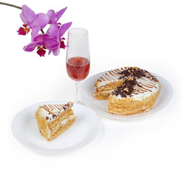 Partly sliced sponge cake, glass of red wine against orchid