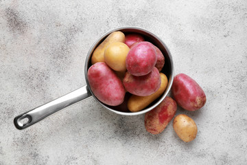 Saucepan with raw potatoes on grey background