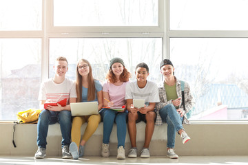 Teenagers with modern devices sitting on window sill