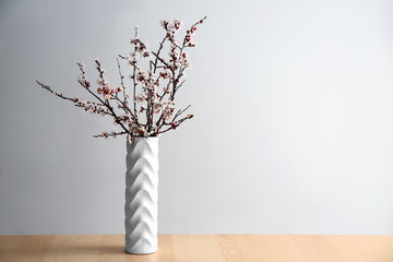 Vase with beautiful blossoming branches on table against light background