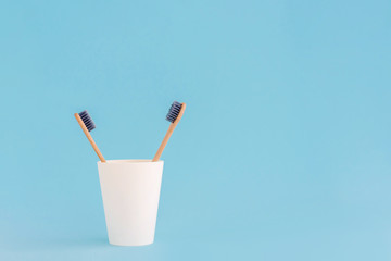 Two wooden toothbrushes in cup on blue background.