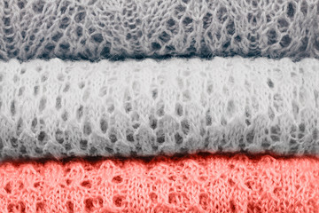 Stylish knitted pastel colored sweaters and one in color of the year 2019 folded in stack. Close up, copy space.