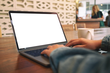 Mockup image of a woman using and typing on laptop with blank white screen and coffee cup on wooden table