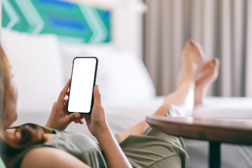 Mockup image of a woman holding and using mobile phone with blank screen while relaxing and lying on the bed
