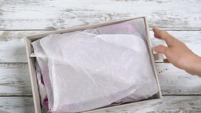 Woman unboxing a freshly received box containing a pair of pink sandals bought from online fashion store. Close-up.