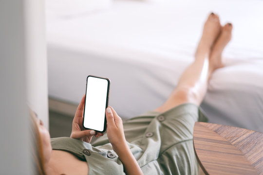 Mockup image of a woman holding and using mobile phone with blank screen while relaxing and lying on the bed