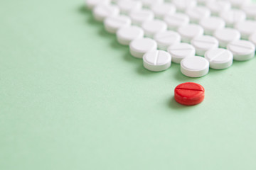 Top view of a pile of white medicine pills on a white surface. One tablet of red medication....