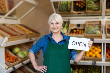 Senior woman holding open sign in organic produce shop