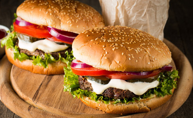 Close-up photo of home made hamburger with beer made of beef, onion, tomato, lettuce, cheese and spices. Fresh burger closeup on wooden rustic table with potato fries and chips.