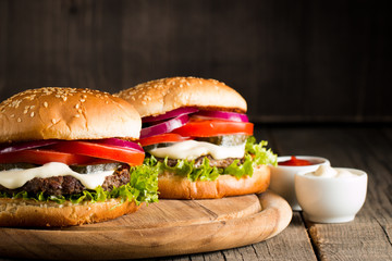 Close-up photo of home made hamburger with beer made of beef, onion, tomato, lettuce, cheese and spices. Fresh burger closeup on wooden rustic table with potato fries and chips.