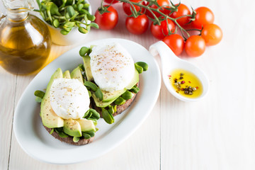 Avocado toast, cherry tomato on wooden background. Breakfast with toast avocado, vegetarian food, healthy diet concept. Healthy sandwich with avocado and poached eggs.