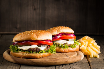 Close-up photo of home made hamburger with beer made of beef, onion, tomato, lettuce, cheese and spices. Fresh burger closeup on wooden rustic table with potato fries and chips.
