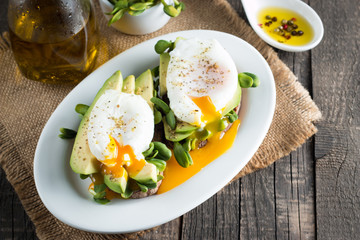 Avocado toast, cherry tomato on wooden background. Breakfast with toast avocado, vegetarian food, healthy diet concept. Healthy sandwich with avocado and poached eggs.
