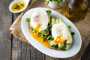Avocado toast, cherry tomato on wooden background. Breakfast with toast avocado, vegetarian food, healthy diet concept. Healthy sandwich with avocado and poached eggs.