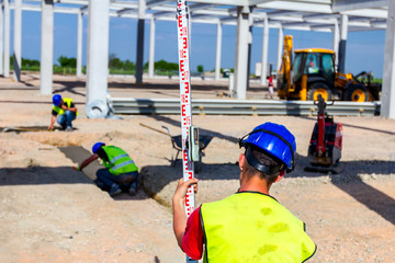 Worker is holding leveling rod to measuring level on construction site