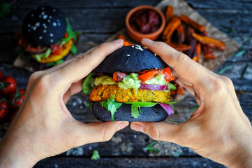 Hands holding fresh chickpea black vegan burger