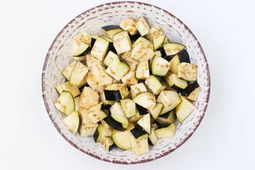 Eggplant cut into cubes for salad, placed in a plate on a white background, top view