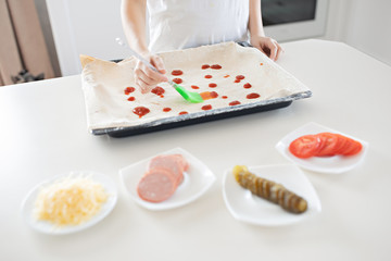 A child prepares Italian pizza at home kitchen. The child lubricates the dough with ketchup. Children's concept chef. Lifestyle, frank moment