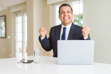 Middle age business man working with computer laptop celebrating surprised and amazed for success with arms raised and open eyes. Winner concept.