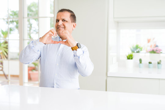 Middle age man sitting at home smiling in love showing heart symbol and shape with hands. Romantic concept.