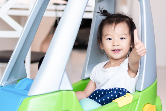 Happy Sweet Little Asian girl riding on small car with thumb up isolated on white