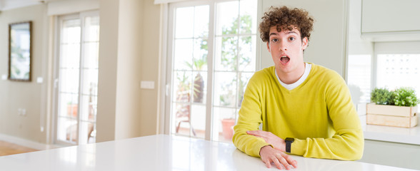 Wide angle shot of young handsome man at home afraid and shocked with surprise expression, fear and excited face.