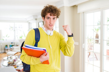 Young student man wearing headphones and backpack holding notebooks annoyed and frustrated shouting with anger, crazy and yelling with raised hand, anger concept