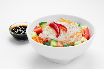 Fresh vegetable salad with soy sauce and sesame seeds in a white plate on a white background.