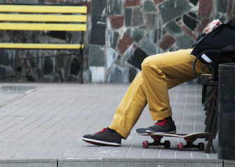 Man Skateboarder in yellow jeans relaxing on bench. Yellow bench and stone background. Lifestyle Relax Hipster Concept