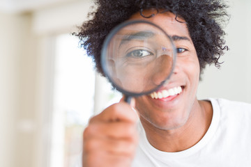 African American man looking through magnifying glass with a happy face standing and smiling with a confident smile showing teeth - obrazy, fototapety, plakaty