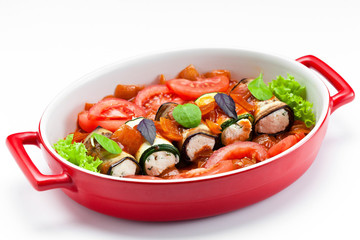 Eggplant with cheese baked with vegetables in a red bowl on a white background.