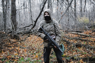 Fototapeta premium Stalker, a guy in uniform and with a gun walks in the yard of an old ruined house in the forest