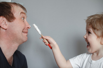 Obraz premium The concept of family. The child draws a brush on the nose of his father. Father and daughter at home having fun
